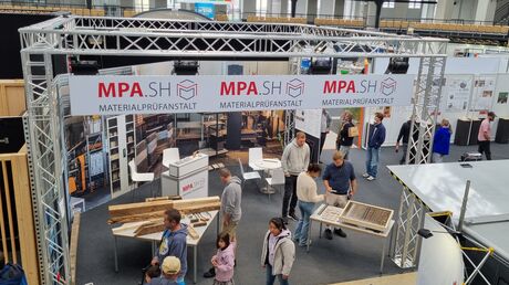 Blick auf einen Messestand der Materialprüfanstalt mit Exponaten und Besucher*innen.