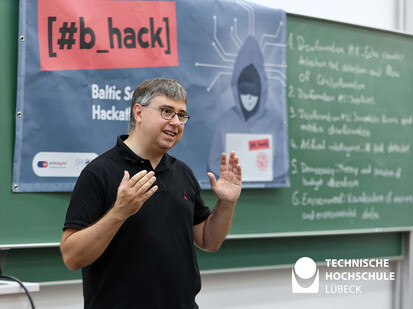 Begrüßung des Informatikfachbereis Dekan Mann steht zum Publikum gerichtet und gestikuliert mit den Händen