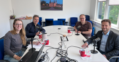 Eine Gruppe von vier Menschen um einen Tisch an Podcastmikrophonen