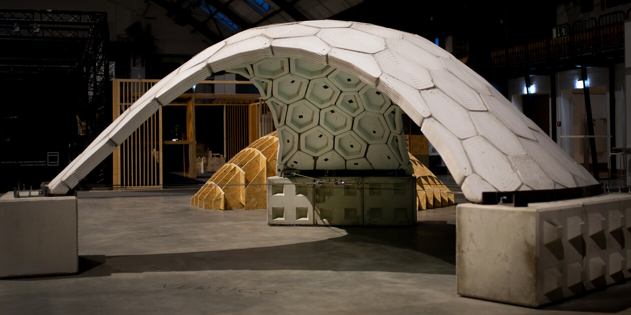Pavillon aus Betonplatten Großer, gebogener Pavillon aus sechseckigen Betonelementen in einer Ausstellungshalle.