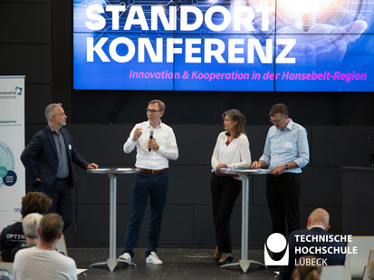 Diskussionsrunde Vier Menschen stehen an jeweils zwei Stehtischen und diskutieren miteinander