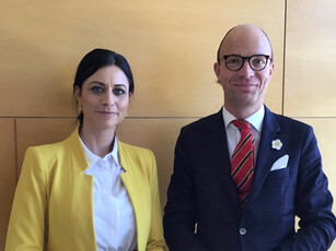 Portrait of a woman in a yellow blazer and a man in a suit and glasses.