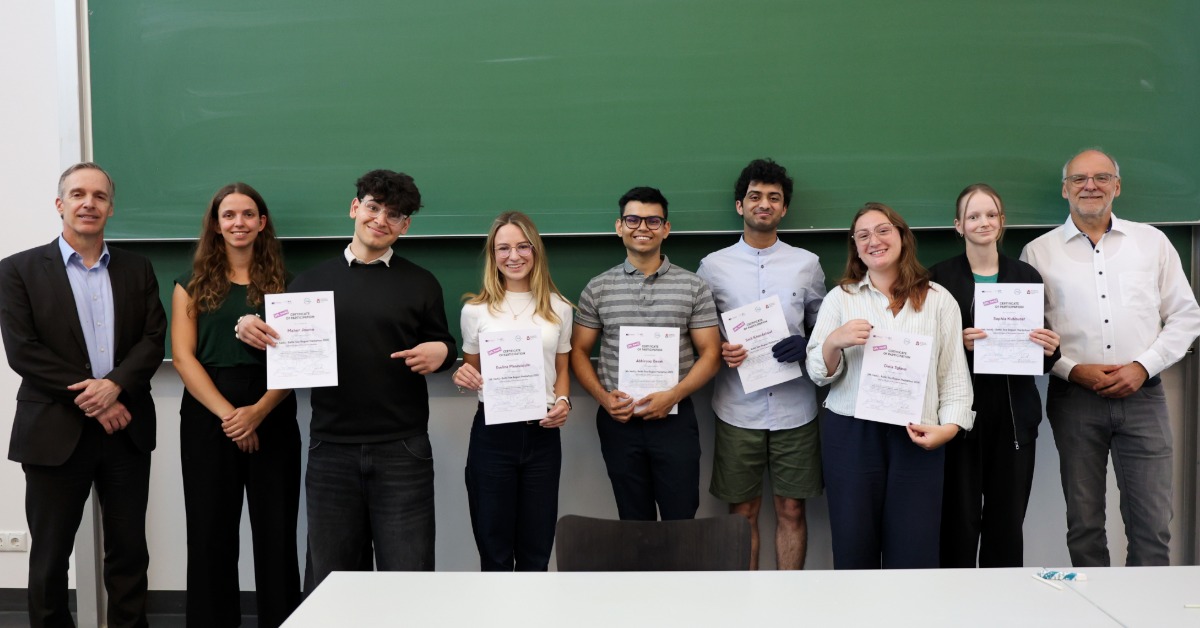 Ein Team steht mit den Organisatoren und Zertifikaten in den Händen vor einer grünen Tafel