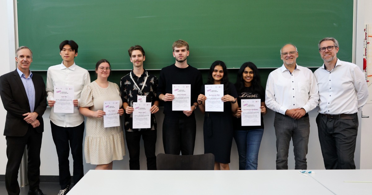 Ein Team steht mit den Organisatoren und Zertifikaten in den Händen vor einer grünen Tafel