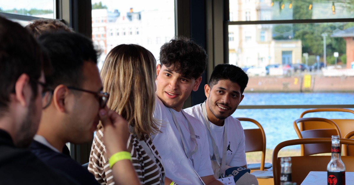 Teilnehmende sitzen an einem Tisch mit Blick auf den Hafen