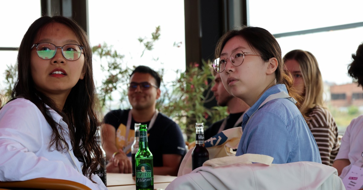 Zwei Teilnehmerinnen mit Brille sitzen an einem Tisch und hören zu