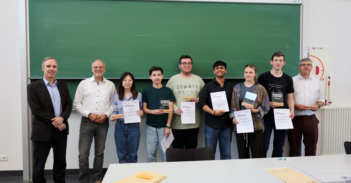 Die Gewinner*innen des Hackathons stehen mit ihren Auszeichnungen vor einer grünen Tafel