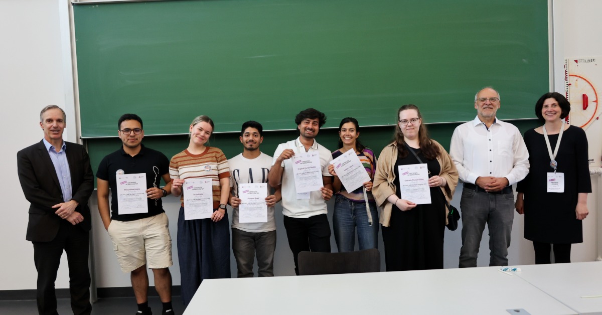 Das Team „Fake News“ mit sechs Teilnehmenden und ihren Zertifikaten steht zwischen den Organisatoren vor einer grünen Tafel.