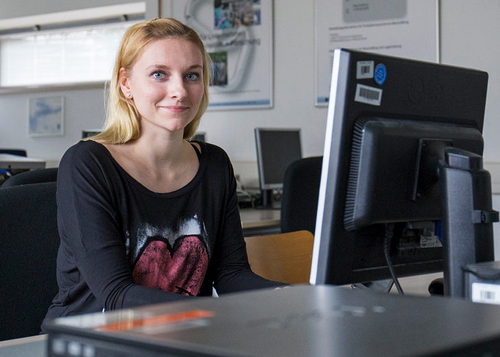 Frau sitzt vor Monitor und lächelt in die Kamera