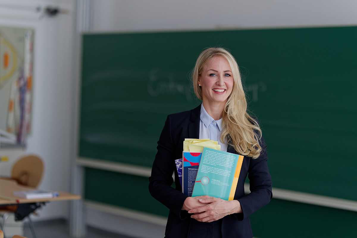 Foto Promovendin Lächelnde Frau mit langen blonden Haaren hält Bücher fest