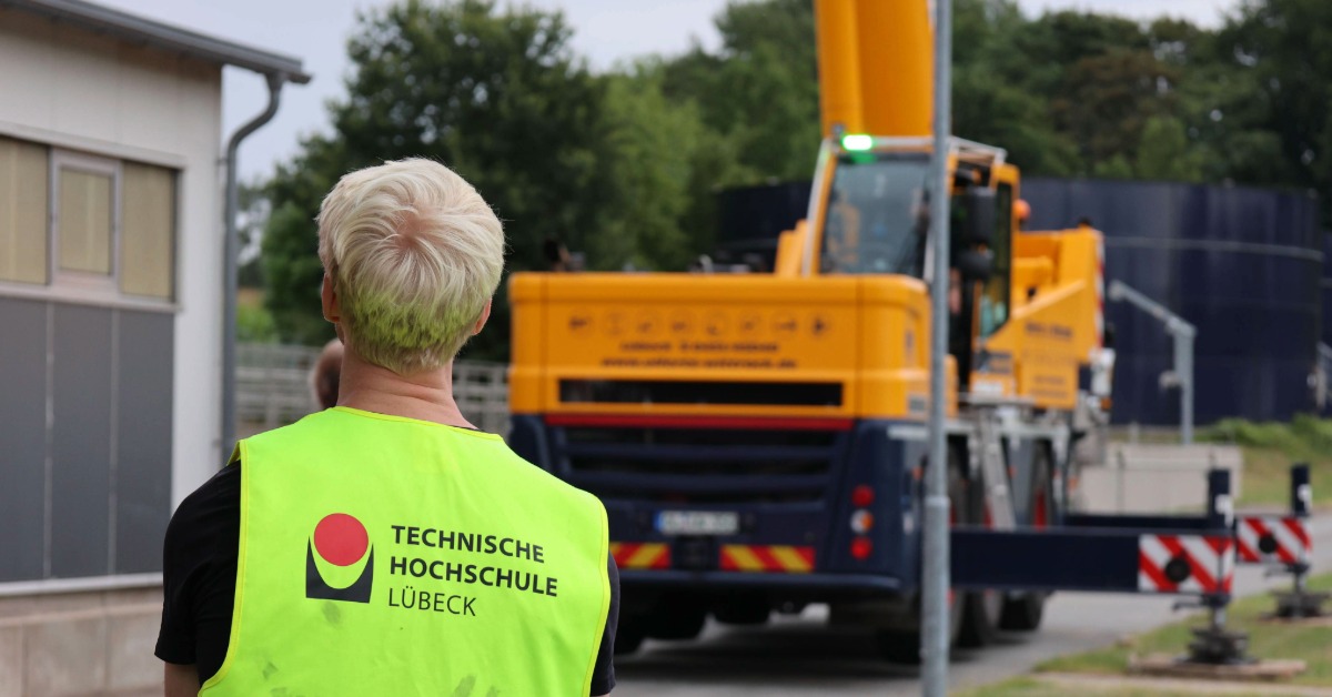 Hinteransicht eines Mannes mit TH-Lübeck-Warnweste vor einem Kran