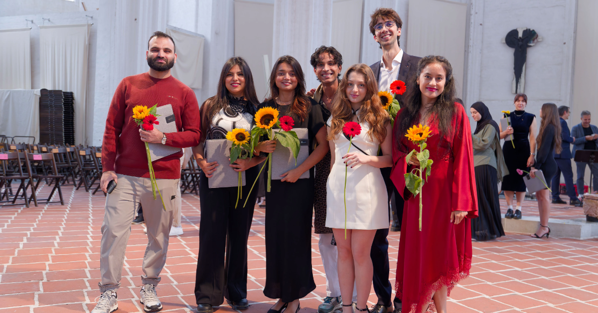 Eine Gruppe von Absolvent*innen lächelt mit Blumen in der Hand in die Kamera.