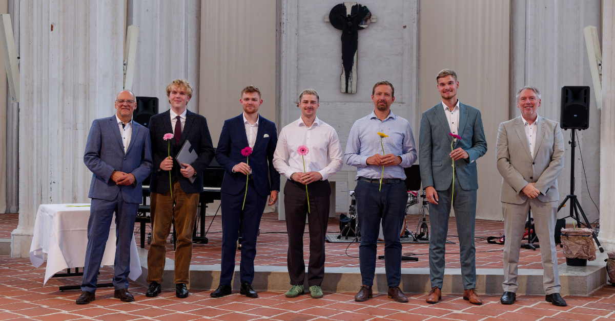 Die Absolvent*innen, der Vizepräsident und der Dekan lächeln in die Kamera.