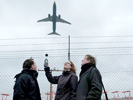 Drei Personen messen mit einem Gerät Lärm der Flugzeuge