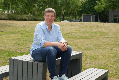 Frau im hellblauen Hemd sitzt auf einer modernen Bank im Grünen.