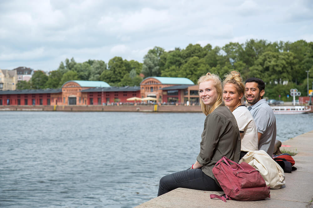 Studierende sitzen bei gutem Wetter an der Hafenkante an der Obertrave
