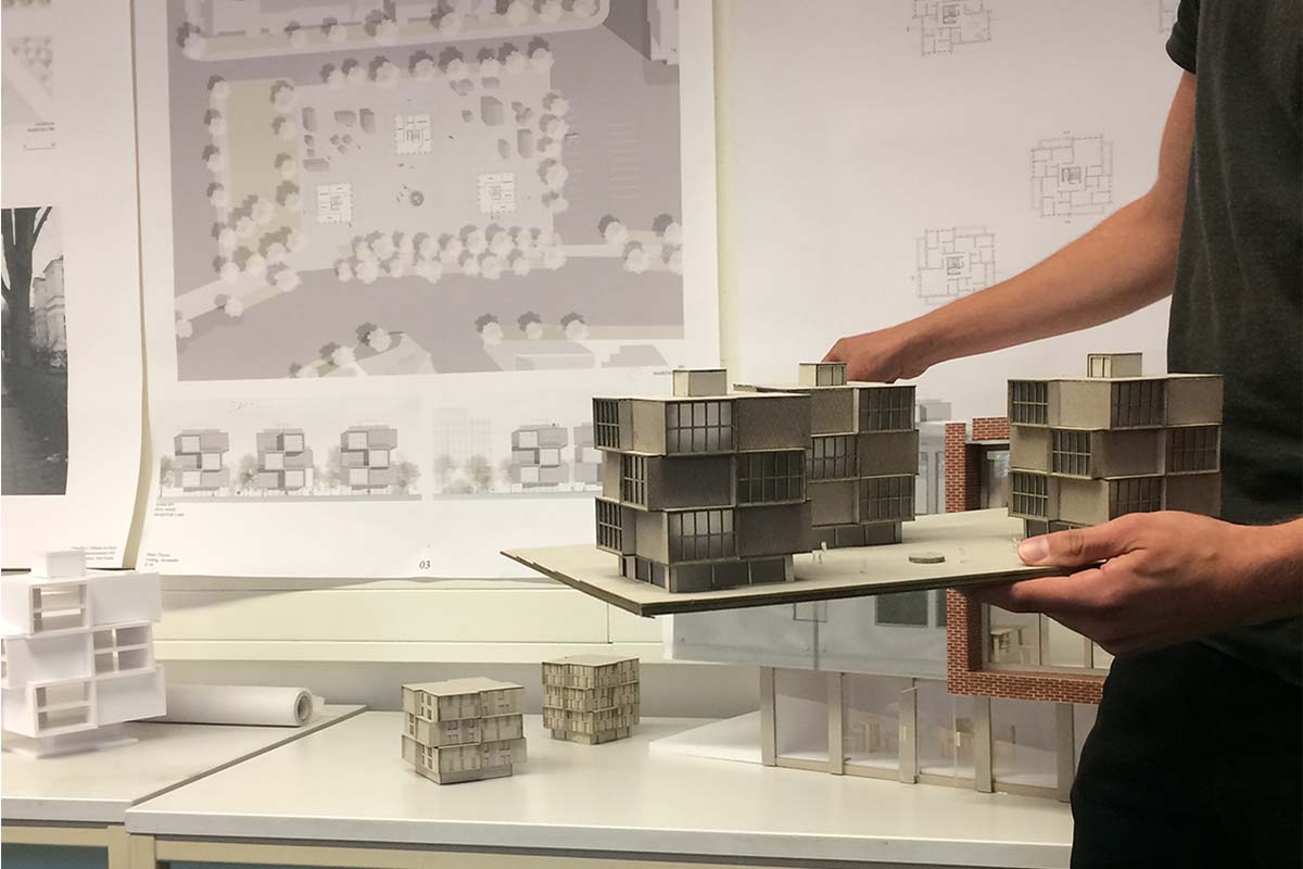 Eine Person hält ein detailliertes Architekturmodell eines mehrstöckigen Gebäudes.