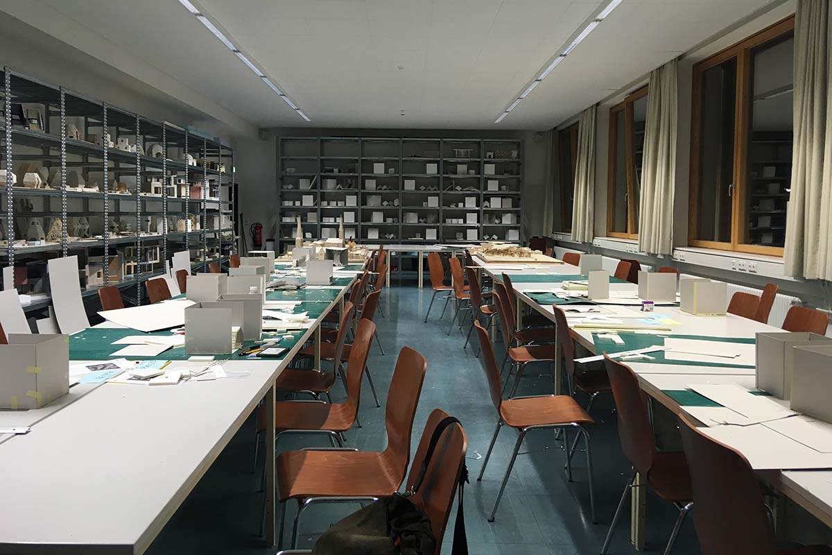 Ein leeres Architektur-Atelier mit langen Tischen und Regalen voller Modelle.