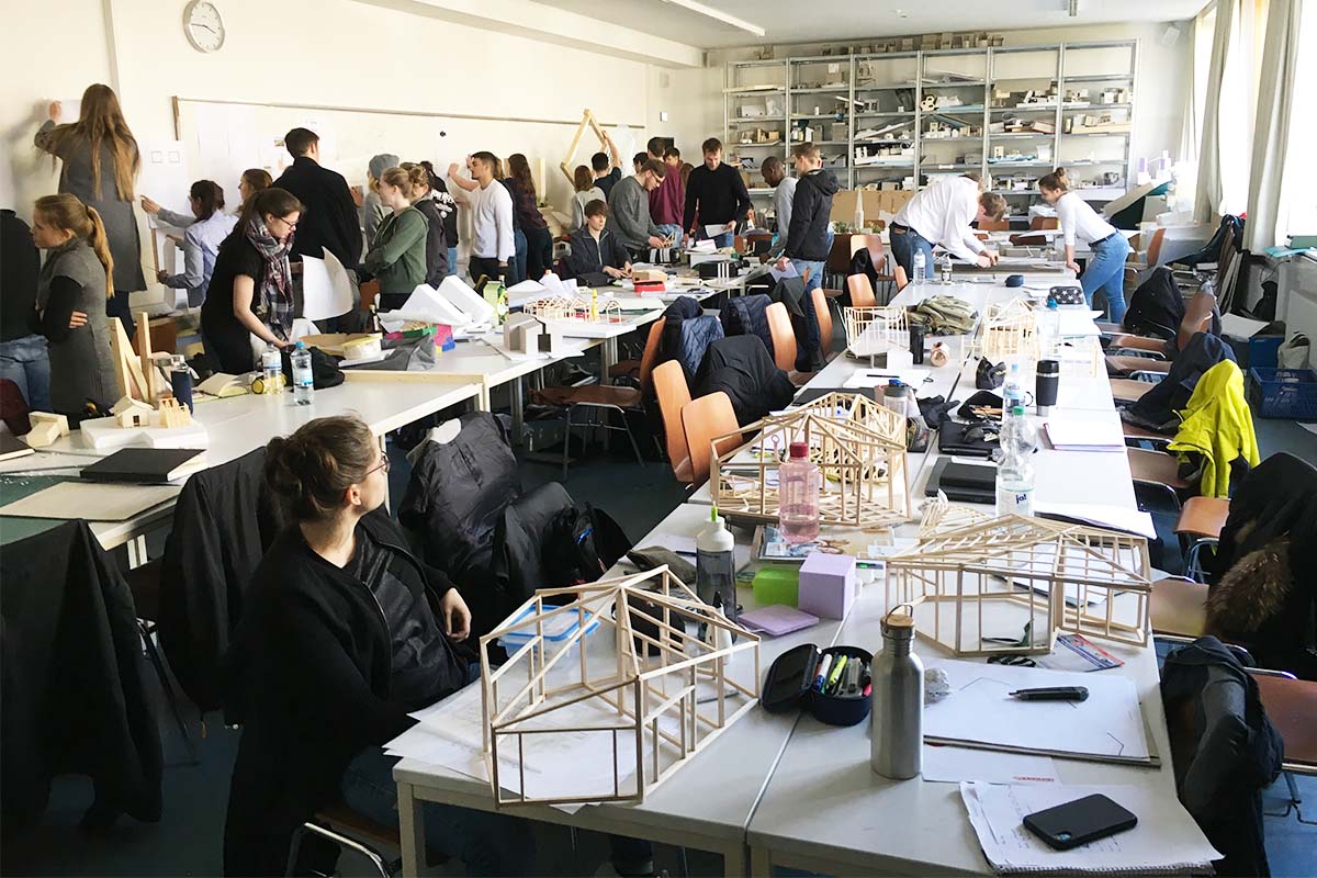 Studierende bauen in einem belebten Atelier an Holzrahmen-Architekturmodellen.