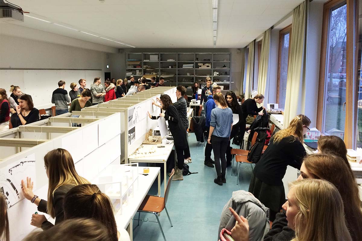 Studierende präsentieren ihre Arbeiten an Ausstellungswänden in einem Atelier.