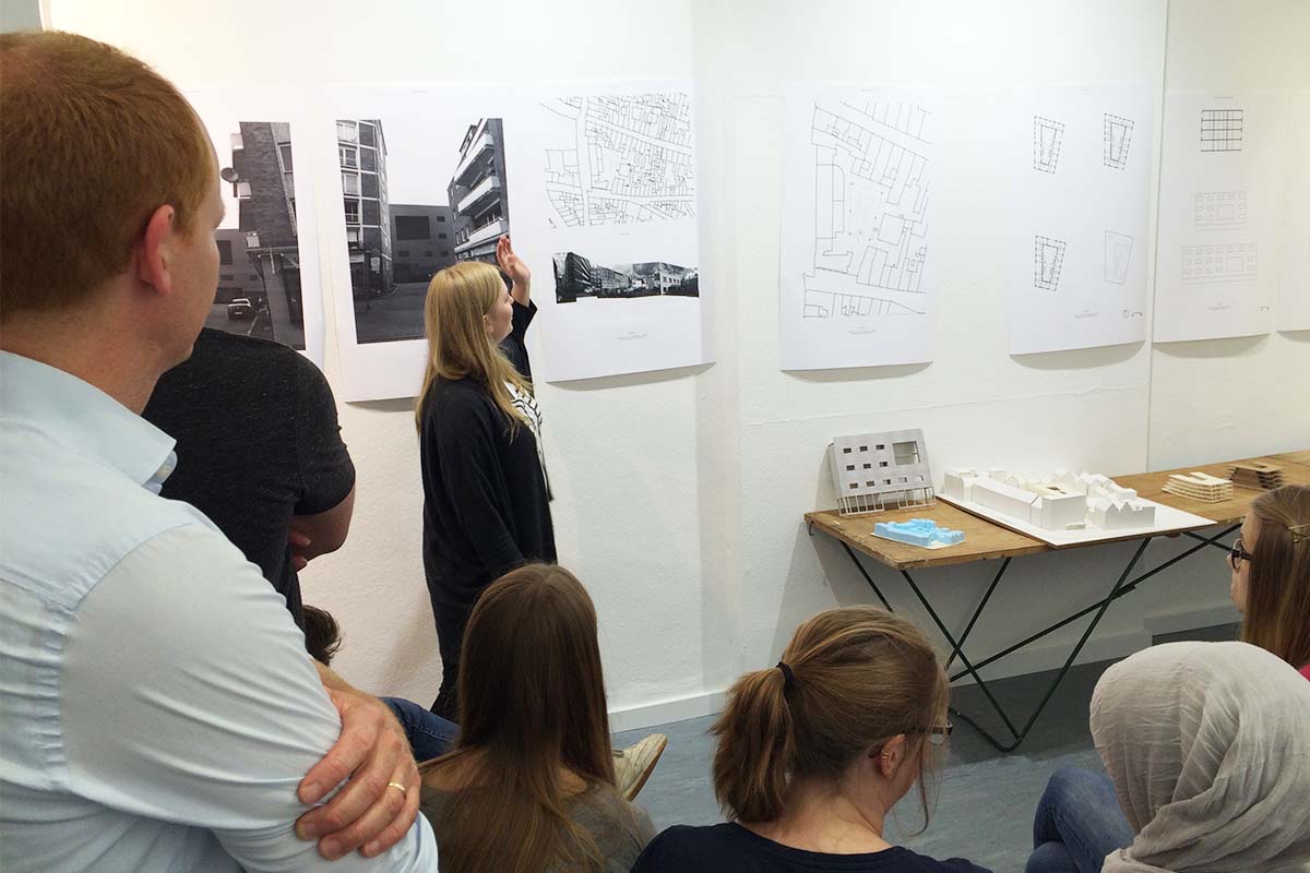 Eine Studentin präsentiert Architekturzeichnungen und Modelle vor einer Gruppe.