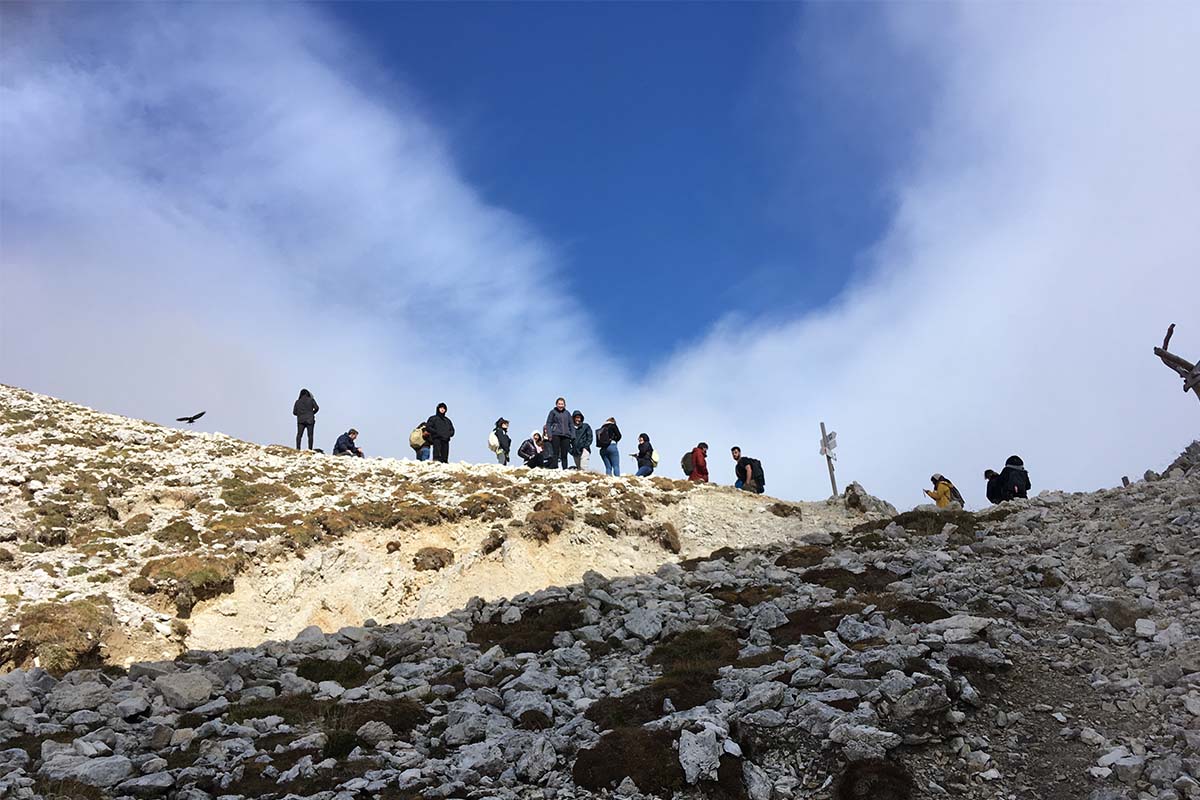 Gruppe wandert über einen felsigen Grat vor blauem Himmel.