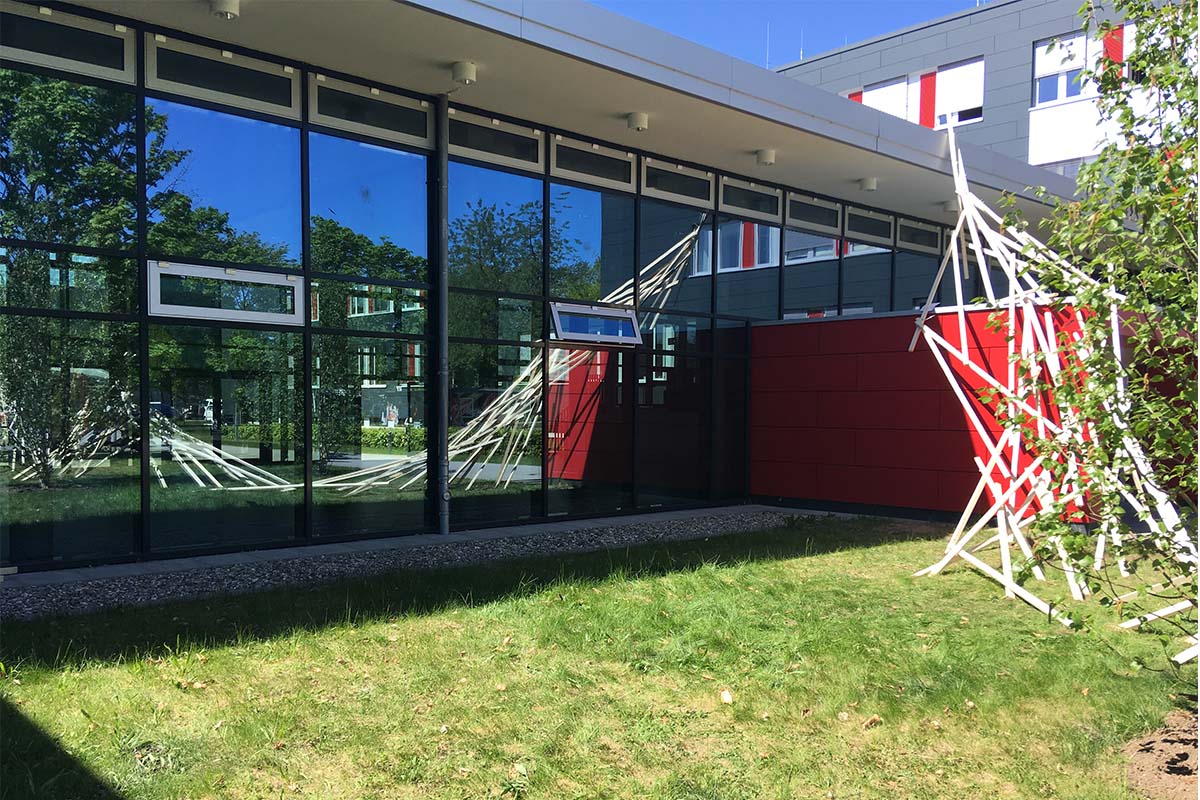 Installation aus Holzlatten vor der Glasfassade eines modernen Gebäudes.