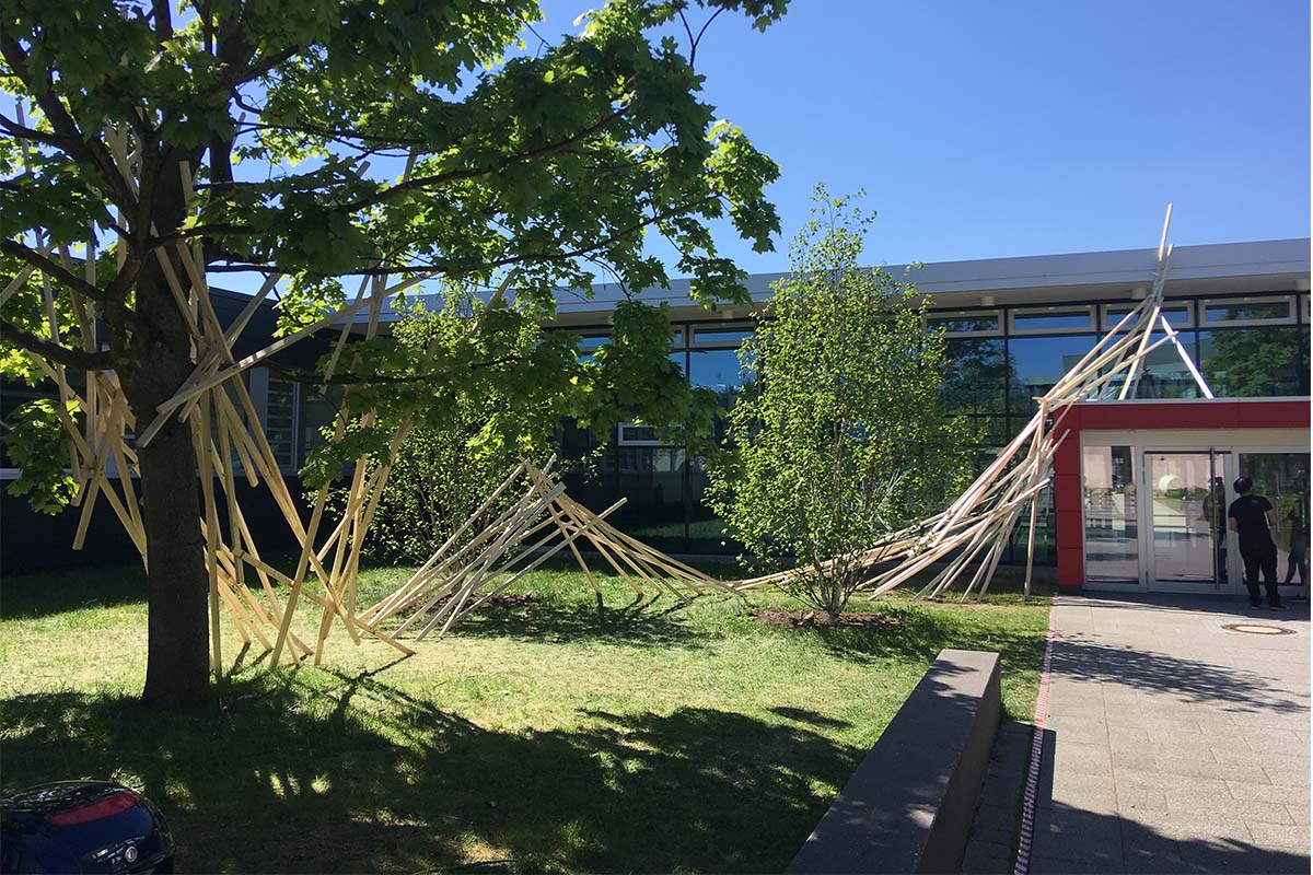 Die Holzkonstruktion verbindet einen Baum mit dem Eingang des Gebäudes.