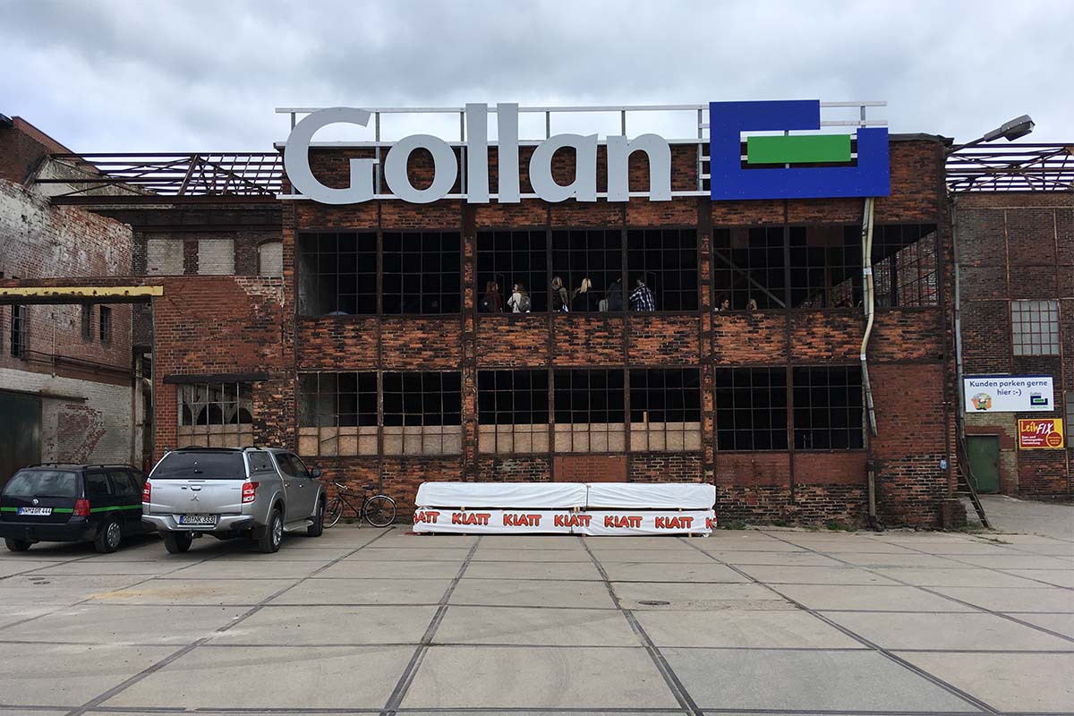 Altes Fabrikgebäude aus Backstein mit großem Gollan-Schriftzug und Besuchern.