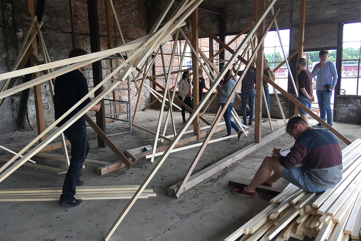 Studierende errichten eine große Holzinstallation in einer alten Industriehalle.