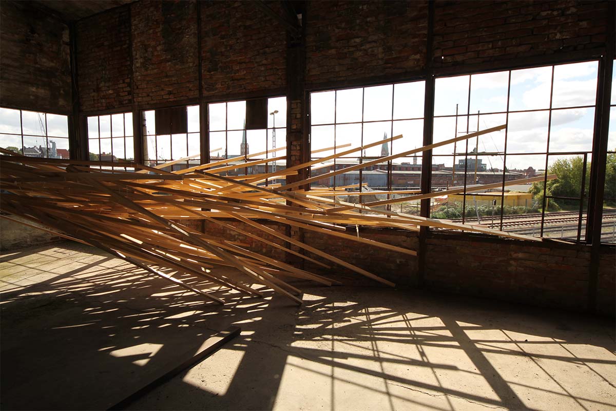 Holzinstallation vor der Fensterfront wirft komplexe Schatten auf den Boden.