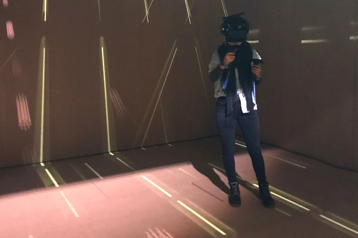 Person mit VR-Brille steht in dunklem Raum mit projizierten Lichtlinien.