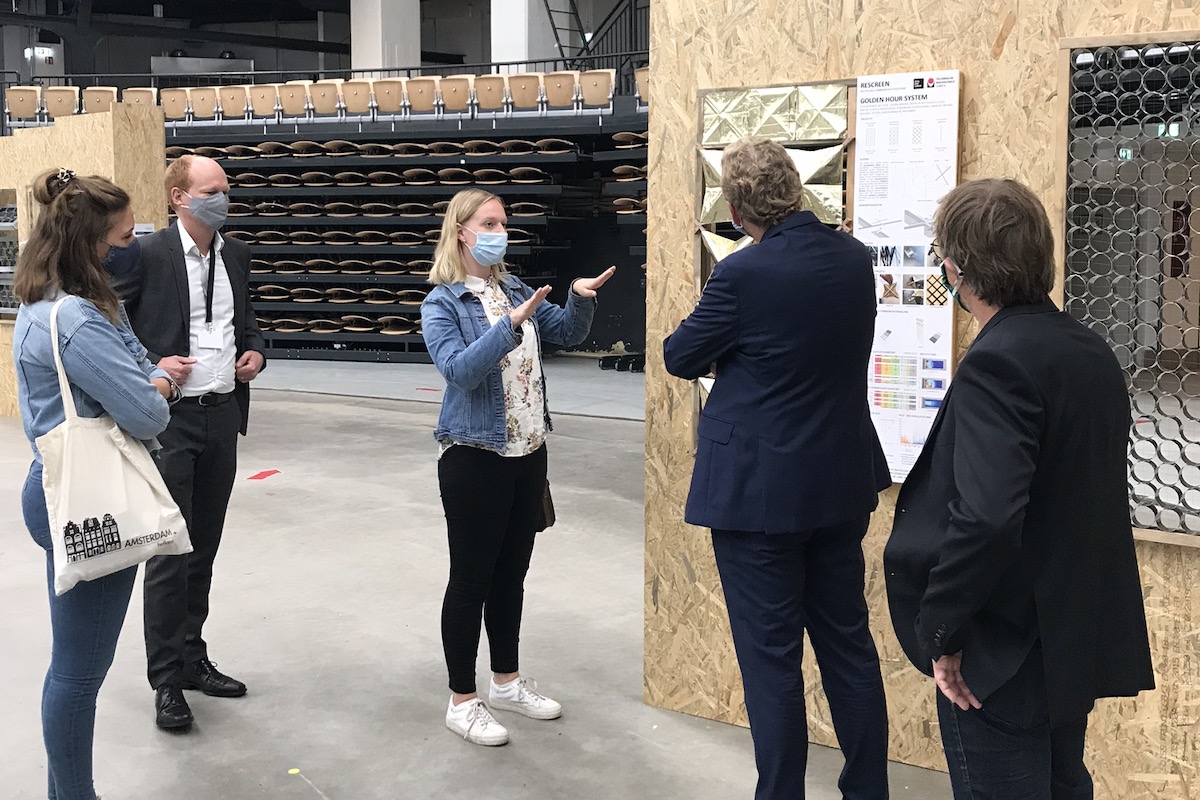 Studentin präsentiert gestikulierend ihren Entwurf vor einer Delegation.