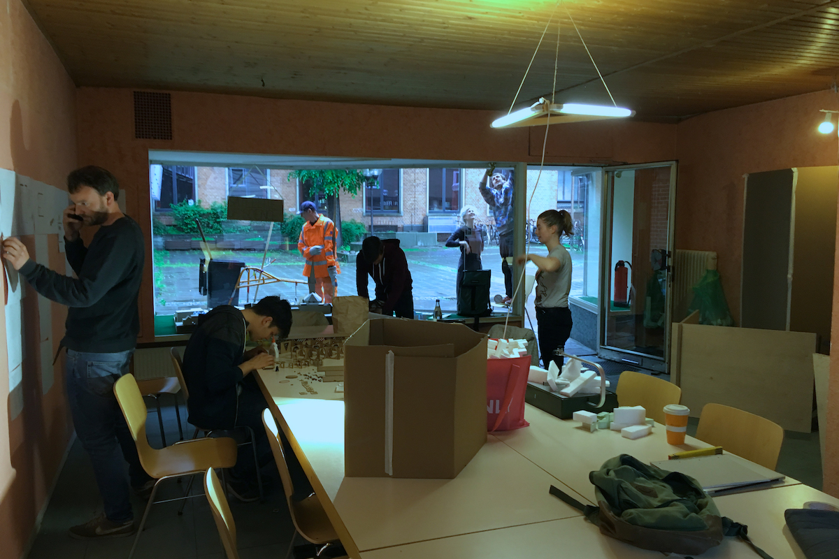 Workshop-Szene: Personen arbeiten an Modellen und Plänen im hellen Raum.