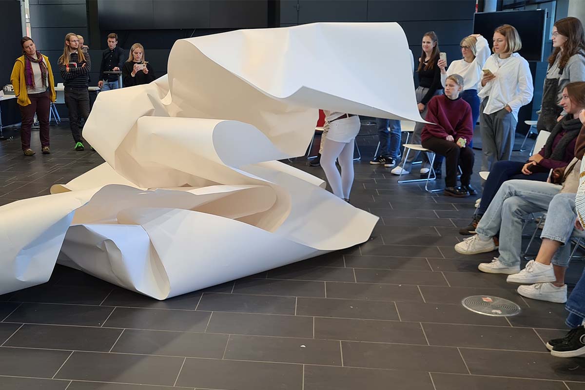 Studierende präsentieren eine große, abstrakte Skulptur aus weißem Papier.