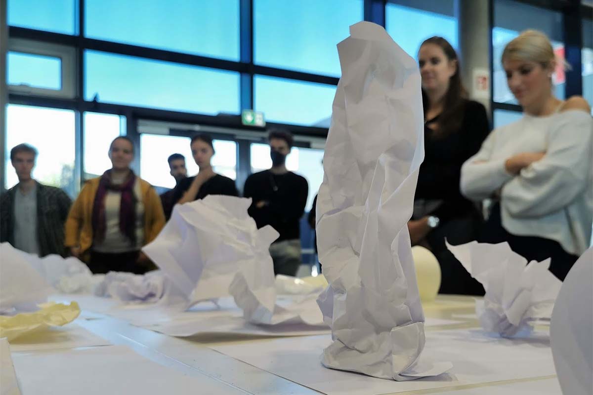 Nahaufnahme kleiner, gefalteter Papiermodelle vor unscharfer Gruppe.