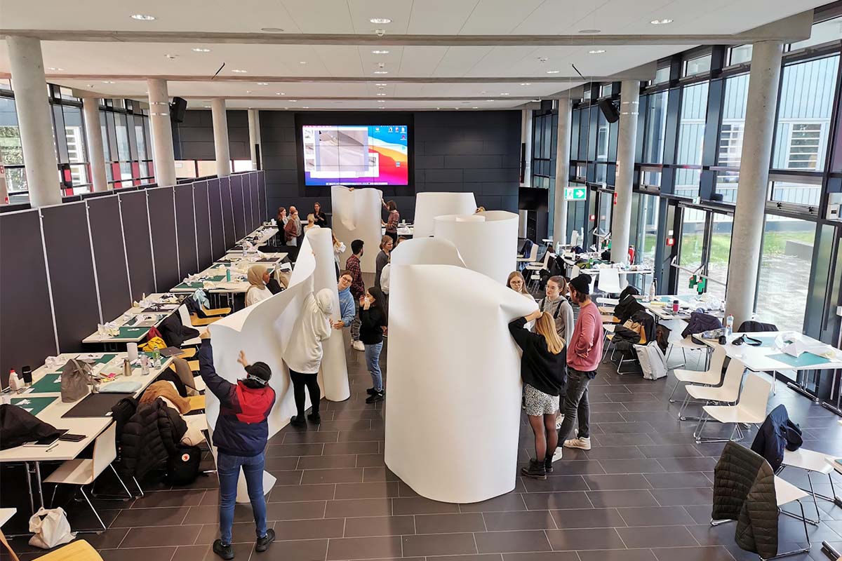 Studierende bauen im Foyer große, stehende Strukturen aus Papierbahnen.