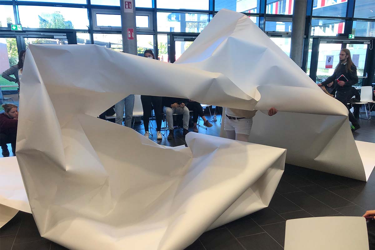 Eine Person stützt eine große, höhlenartige Papierinstallation von innen.