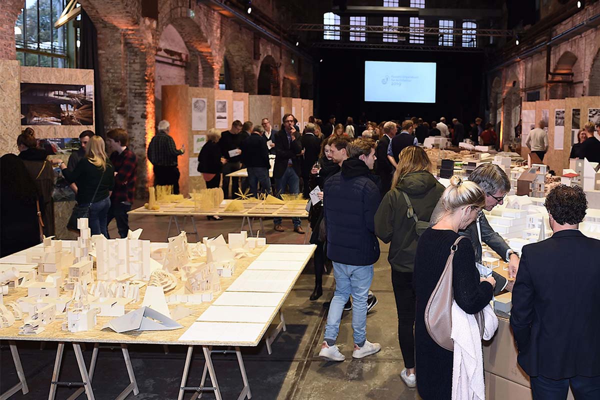 Besucher betrachten Architekturmodelle bei einer Ausstellung in einer großen Halle.