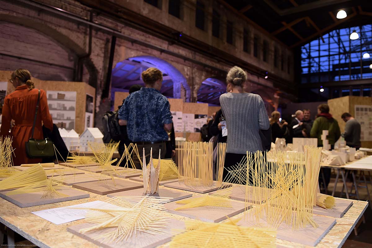 Filigrane Architekturmodelle aus dünnen Holzstäben stehen auf einem Tisch.