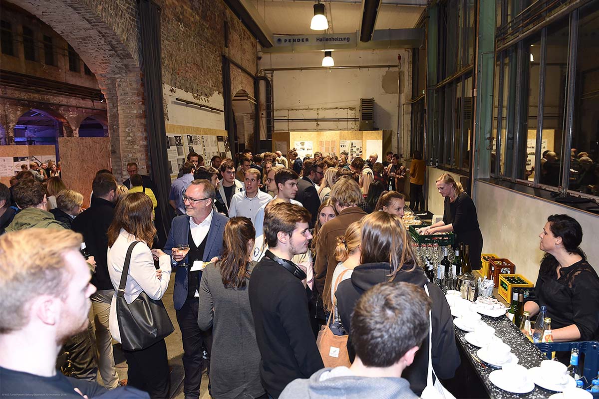 Viele Menschen stehen bei einem Empfang in einem Industrieflur an einer Bar.