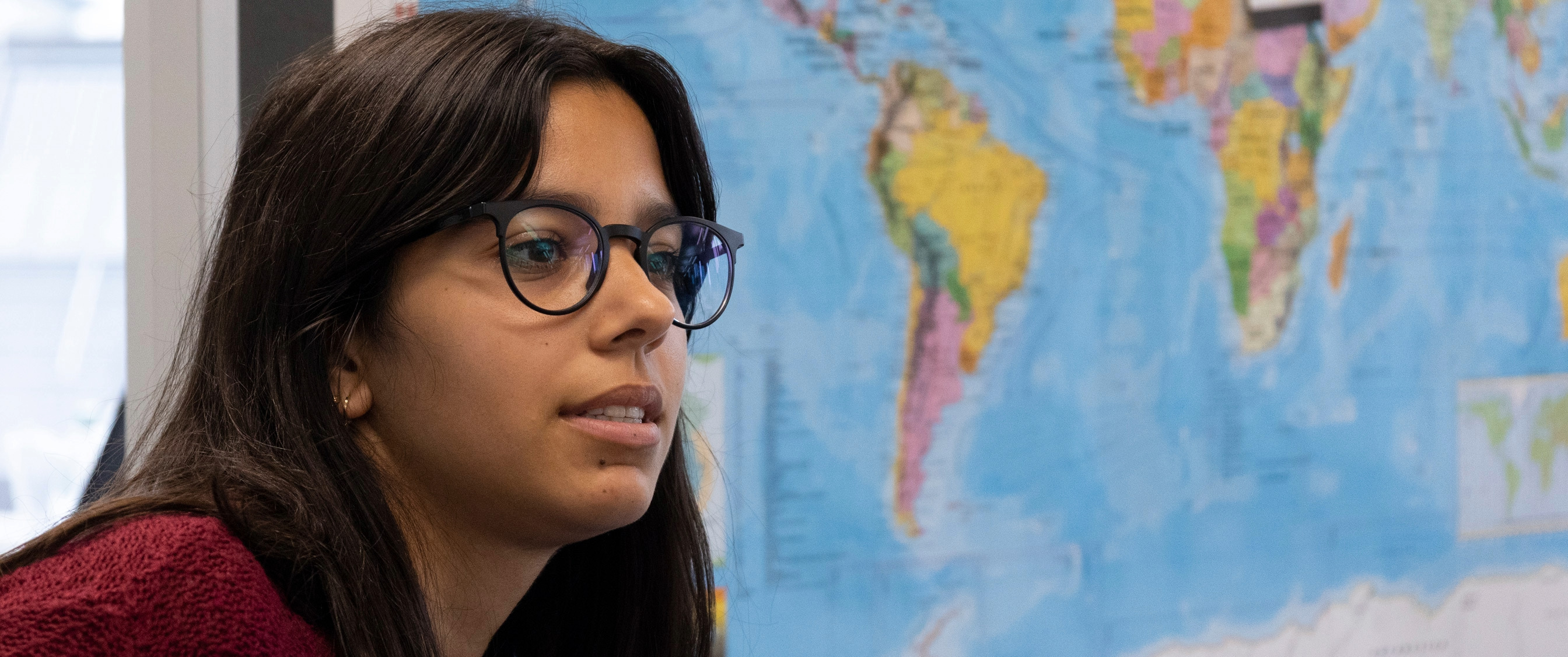 Young woman with glasses in profile in front of a world map