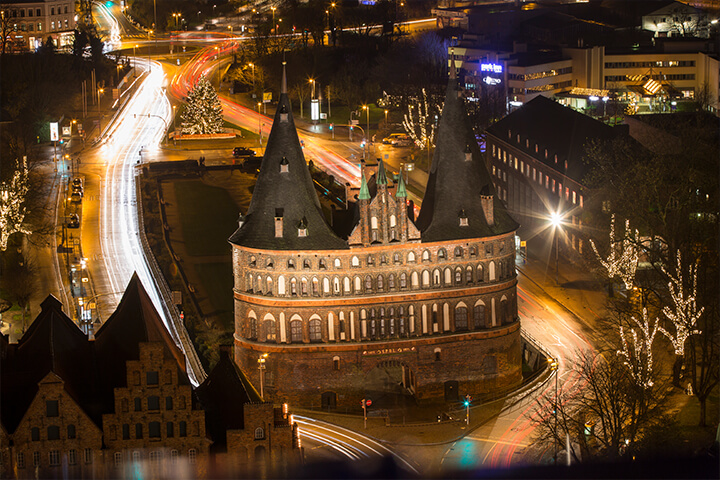 Blick aus dem Aussichtsturm der Hochschulkirche St. Petri auf das Holstentor bei Nacht.