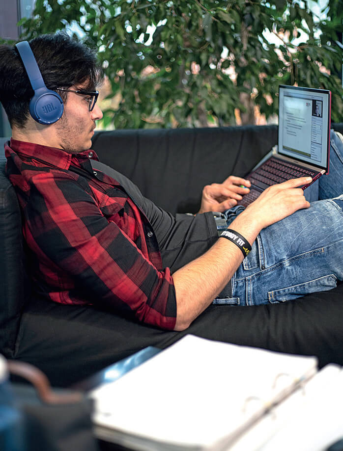 Ein Student der TH Lübeck studiert online mit seinem Laptop auf der Couch liegend