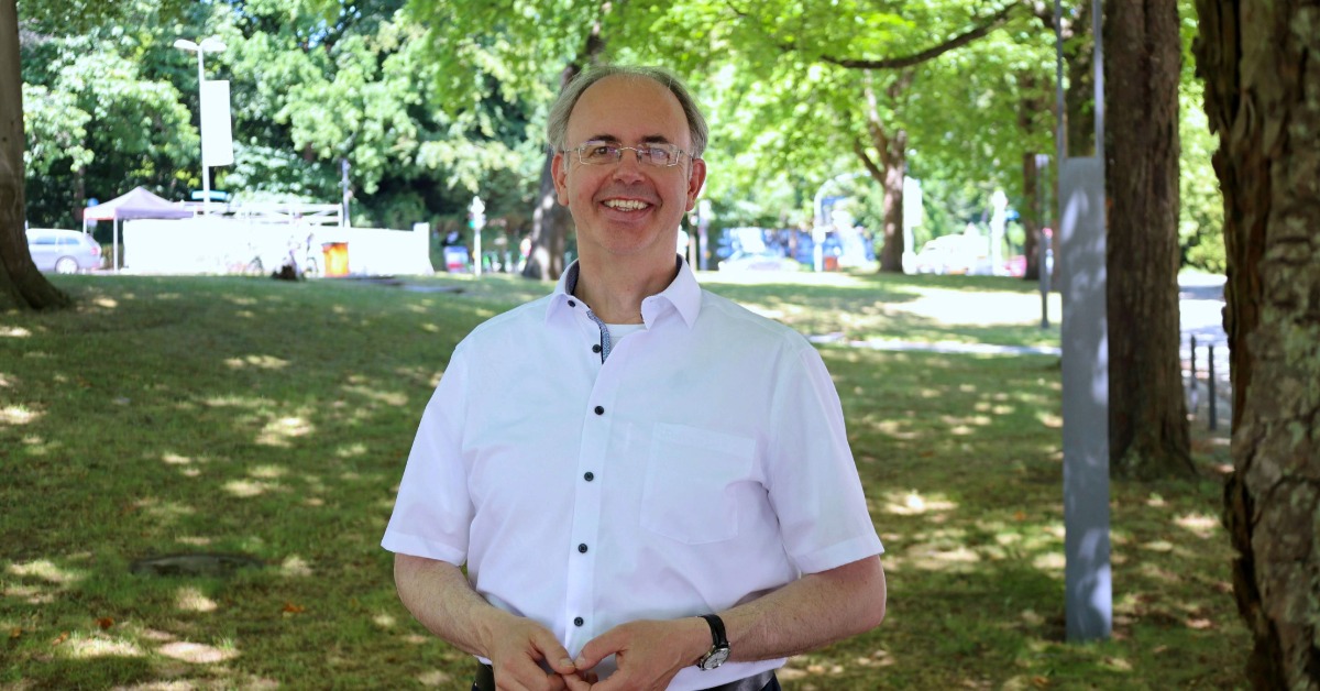 Professor steht draußen im Grünen.
