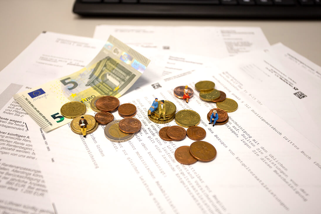 Miniaturfiguren sitzen auf Euromünzen und einem Geldschein, die auf Rentendokumenten liegen