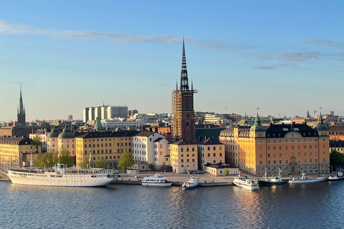 Stockholm Altstadt (Gamla Stan) mit Blick auf die Riddarholmen-Kirche, historische Gebäude am Wasser und Boote im Hafen bei Sonnenuntergang.