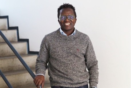 Lächelnder Mann mit Brille steht vor Treppe angelehnt an Geländer